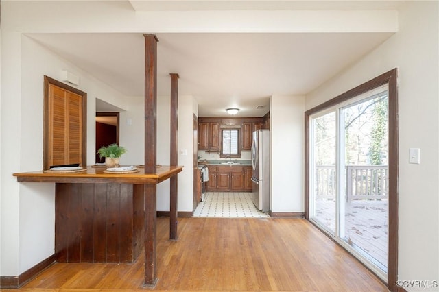 kitchen with kitchen peninsula, stainless steel fridge, a breakfast bar, and light wood-type flooring