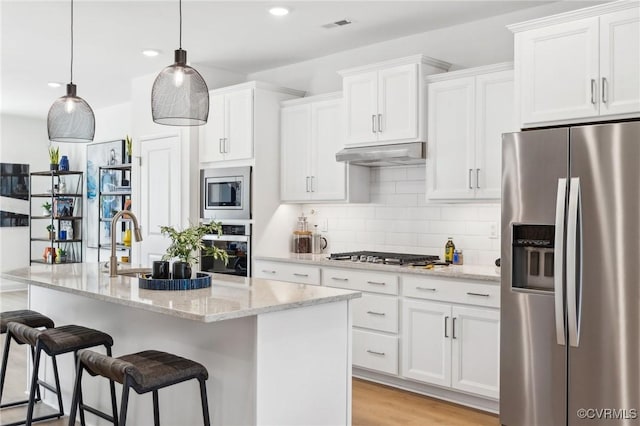 kitchen featuring a center island with sink, decorative light fixtures, light stone counters, white cabinetry, and stainless steel appliances