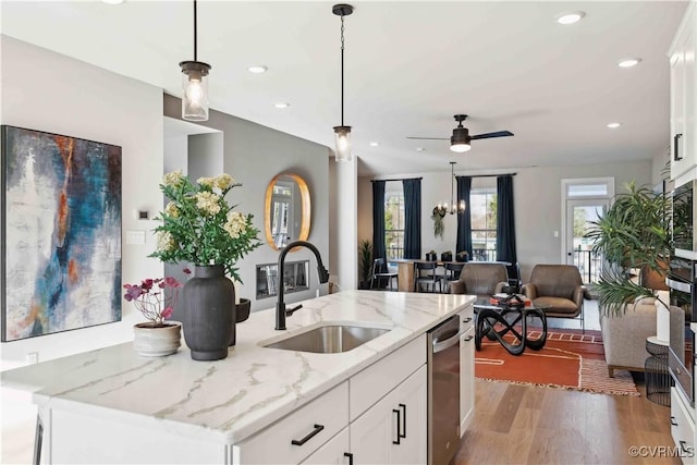 kitchen featuring open floor plan, wood finished floors, decorative light fixtures, a sink, and stainless steel dishwasher