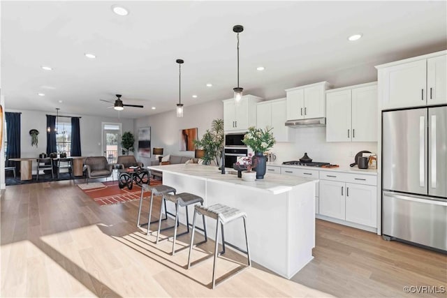 kitchen with light wood-style flooring, stainless steel appliances, under cabinet range hood, a kitchen bar, and white cabinetry