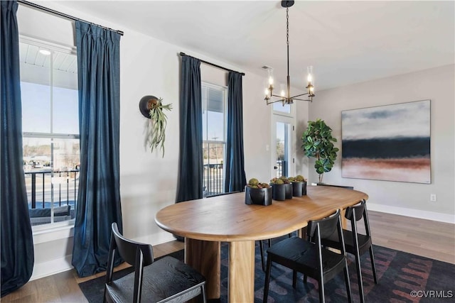 dining area featuring dark wood-style flooring, a notable chandelier, plenty of natural light, and baseboards