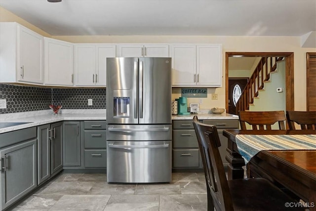 kitchen featuring gray cabinetry, white cabinetry, stainless steel fridge with ice dispenser, light stone counters, and decorative backsplash