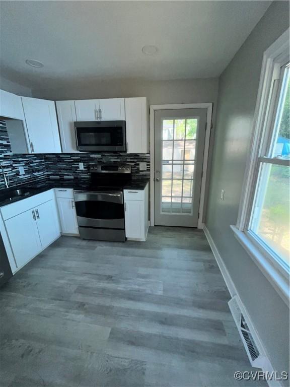 kitchen with white cabinets, backsplash, stainless steel appliances, and light hardwood / wood-style flooring