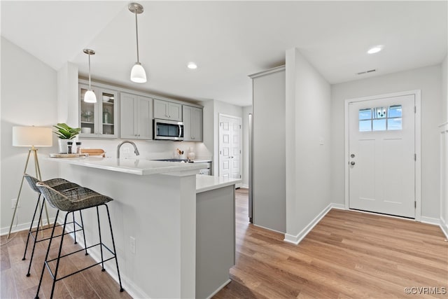 kitchen with kitchen peninsula, light wood-type flooring, a breakfast bar, gray cabinets, and hanging light fixtures