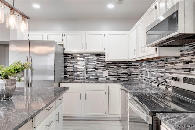 kitchen with white cabinets, decorative light fixtures, stainless steel appliances, and dark stone countertops