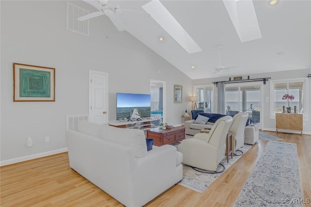 living room with ceiling fan, light wood-type flooring, high vaulted ceiling, and a skylight