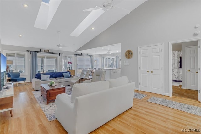 living room featuring ceiling fan, light wood-type flooring, high vaulted ceiling, and a skylight