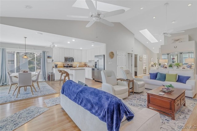 living room with a skylight, ceiling fan, high vaulted ceiling, and light wood-type flooring