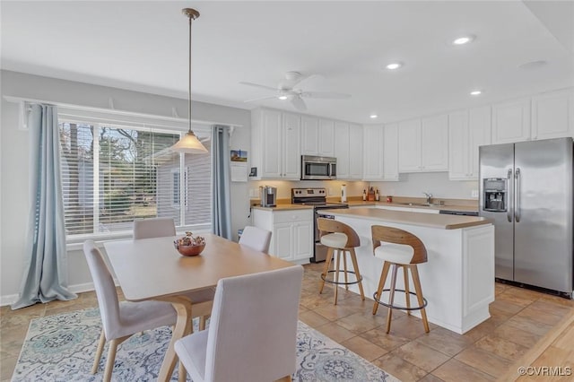 kitchen featuring white cabinets, hanging light fixtures, ceiling fan, appliances with stainless steel finishes, and a kitchen island