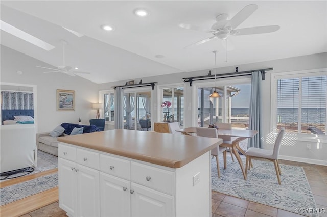 kitchen with a center island, vaulted ceiling with skylight, ceiling fan, light tile patterned floors, and white cabinetry