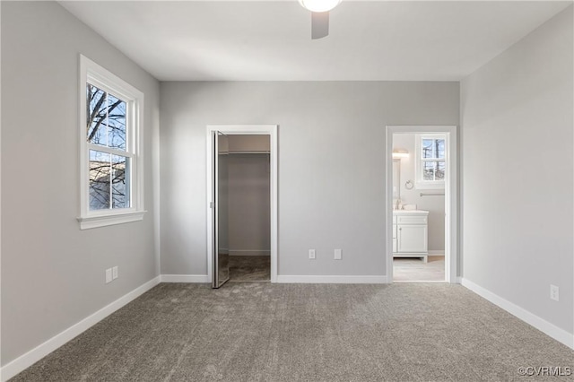 unfurnished bedroom featuring light colored carpet, a walk in closet, multiple windows, and ensuite bath