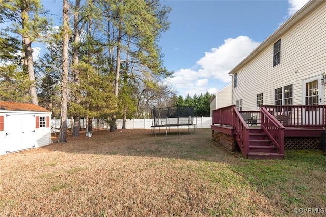 view of yard featuring a trampoline, a wooden deck, an outdoor structure, a fenced backyard, and a shed