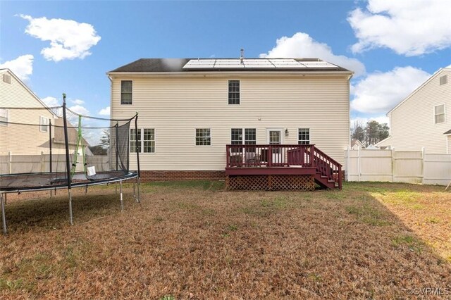 back of house with a lawn, a trampoline, roof mounted solar panels, and a deck