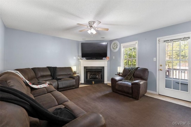 carpeted living area featuring baseboards, a ceiling fan, a fireplace with flush hearth, and a textured ceiling