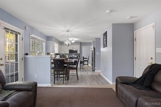 living room with an inviting chandelier, baseboards, light wood-type flooring, and a textured ceiling