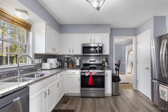 kitchen featuring white cabinets, dark wood-style flooring, a sink, stainless steel appliances, and backsplash