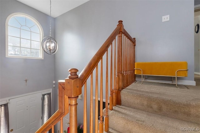 staircase featuring carpet floors, baseboards, and a notable chandelier