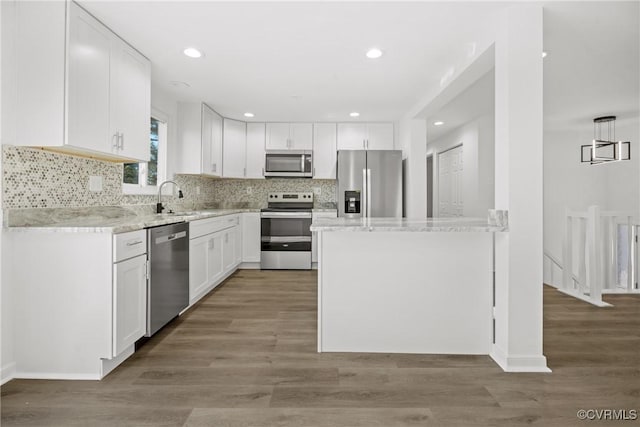 kitchen with appliances with stainless steel finishes, hanging light fixtures, white cabinetry, and light hardwood / wood-style floors