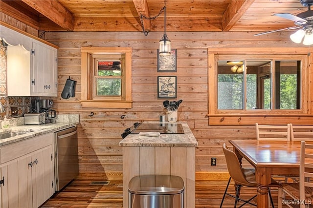 kitchen featuring pendant lighting, hardwood / wood-style floors, stainless steel dishwasher, light stone countertops, and beamed ceiling