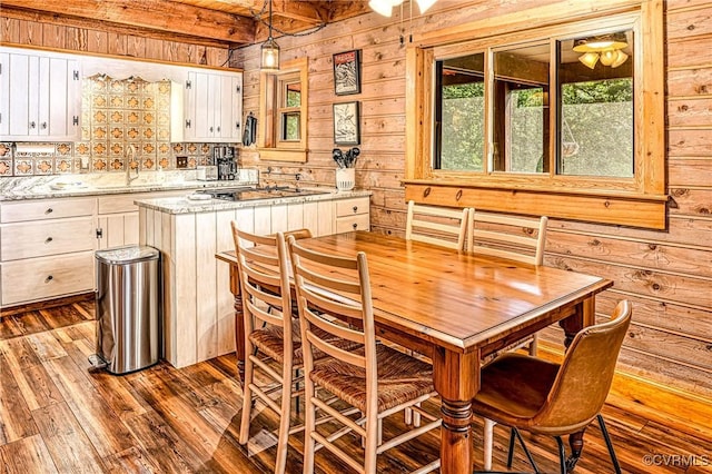 kitchen with white cabinets, sink, wooden walls, hanging light fixtures, and light hardwood / wood-style flooring