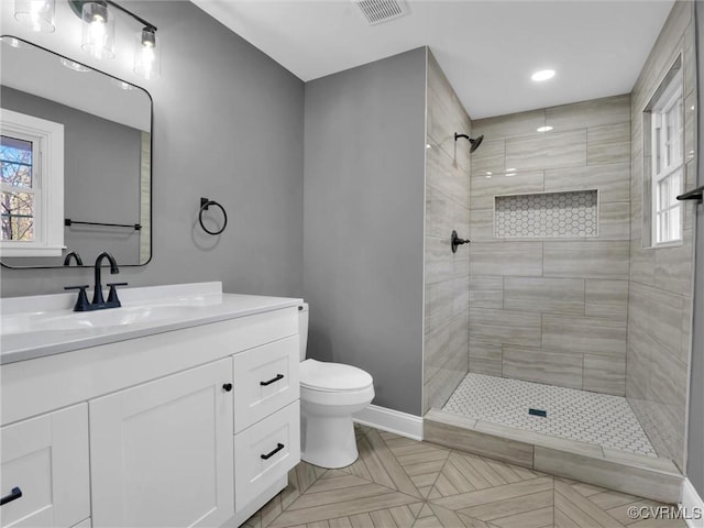 bathroom with a tile shower, vanity, and toilet