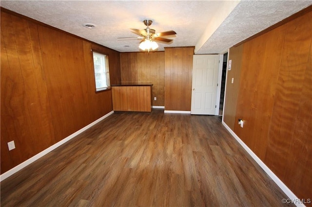 empty room with a textured ceiling, wooden walls, ceiling fan, and dark wood-type flooring