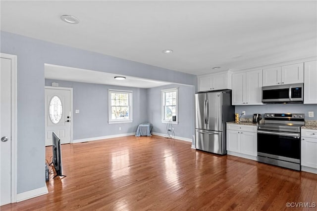 kitchen with hardwood / wood-style flooring, light stone counters, white cabinetry, and stainless steel appliances