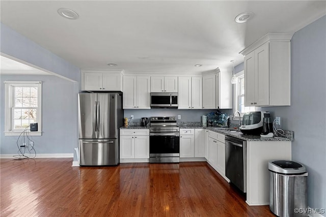 kitchen with appliances with stainless steel finishes, dark stone counters, sink, white cabinets, and dark hardwood / wood-style floors