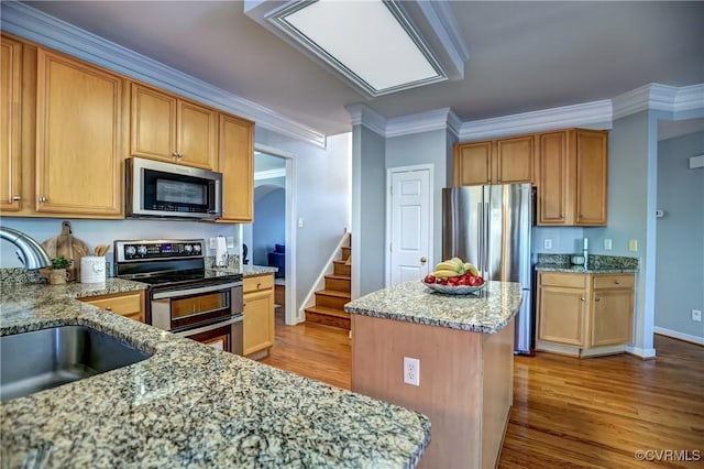 kitchen with sink, light stone counters, appliances with stainless steel finishes, a kitchen island, and ornamental molding