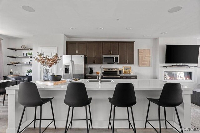 kitchen featuring appliances with stainless steel finishes, light wood-type flooring, a kitchen island with sink, and sink