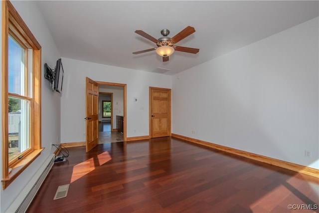 unfurnished room with baseboard heating, ceiling fan, plenty of natural light, and dark wood-type flooring