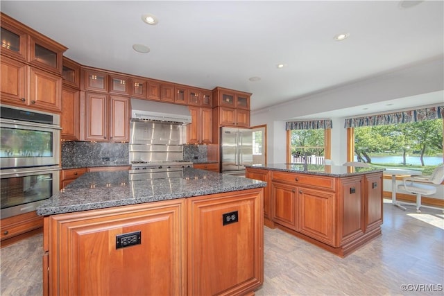 kitchen featuring a center island, exhaust hood, dark stone countertops, tasteful backsplash, and stainless steel appliances