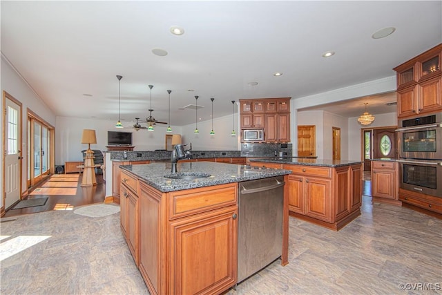 kitchen featuring pendant lighting, sink, dark stone countertops, an island with sink, and appliances with stainless steel finishes