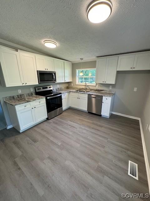 kitchen featuring appliances with stainless steel finishes, light wood-type flooring, a textured ceiling, sink, and white cabinets