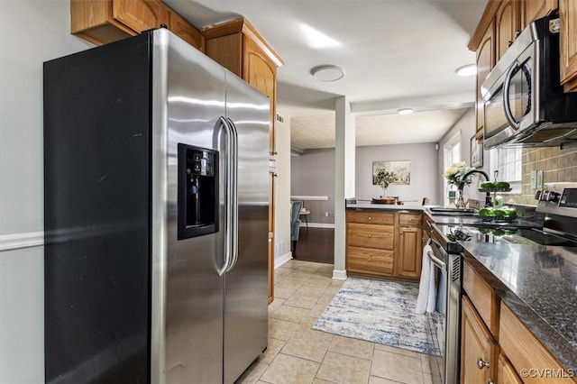 kitchen with decorative backsplash, appliances with stainless steel finishes, dark stone counters, sink, and light tile patterned flooring