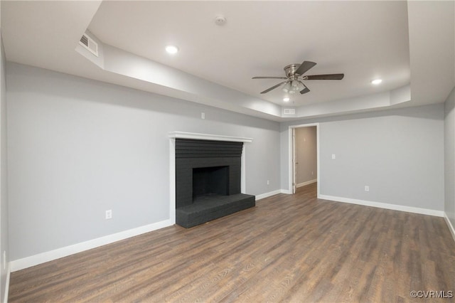 unfurnished living room with a raised ceiling, ceiling fan, dark hardwood / wood-style flooring, and a brick fireplace