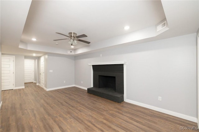 unfurnished living room featuring a brick fireplace, ceiling fan, and dark wood-type flooring