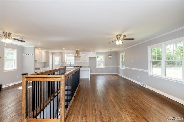 unfurnished living room featuring crown molding, ceiling fan, dark wood-type flooring, and sink