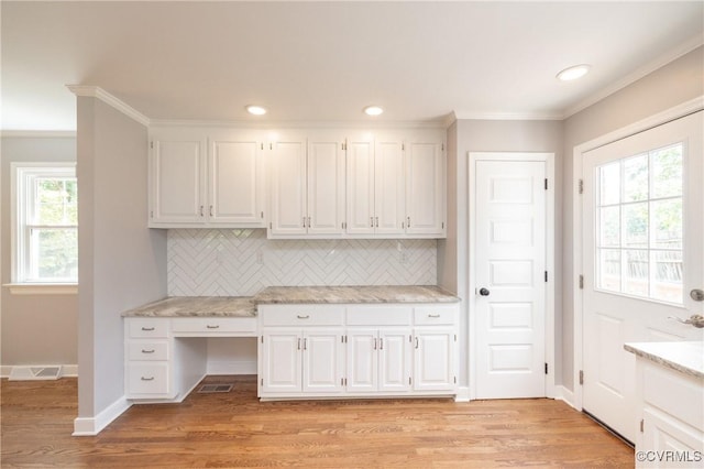 kitchen with light stone countertops, backsplash, ornamental molding, white cabinets, and light hardwood / wood-style floors