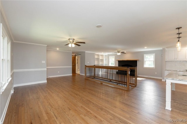 unfurnished living room with a barn door, hardwood / wood-style flooring, ceiling fan, and crown molding