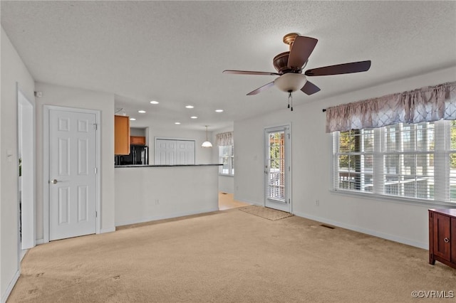 unfurnished living room with ceiling fan, light carpet, and a textured ceiling