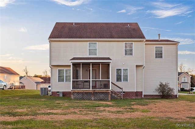 back house at dusk with a sunroom, central AC unit, and a lawn