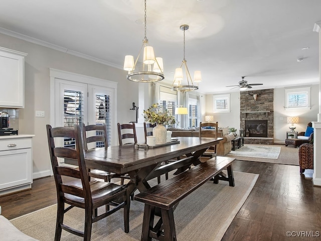 dining area featuring ceiling fan with notable chandelier, dark hardwood / wood-style flooring, a wealth of natural light, and a stone fireplace