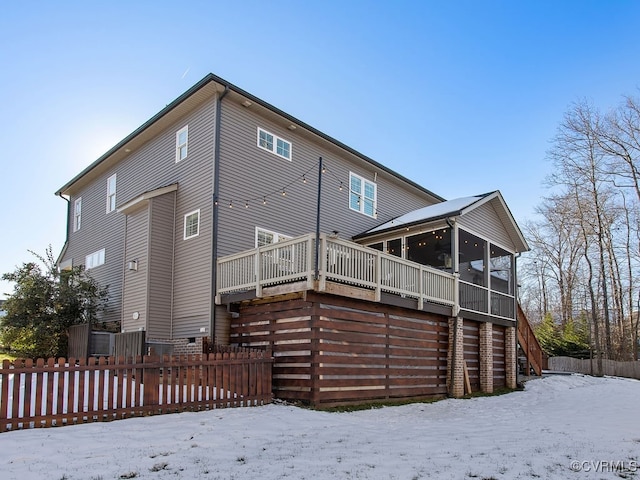 snow covered back of property featuring a wooden deck and a sunroom