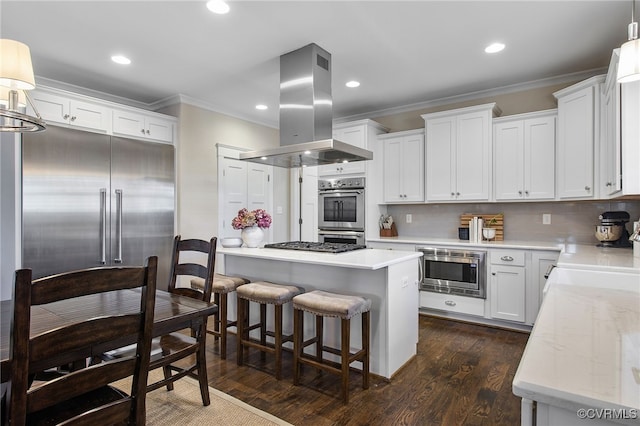 kitchen with built in appliances, white cabinets, island exhaust hood, pendant lighting, and crown molding