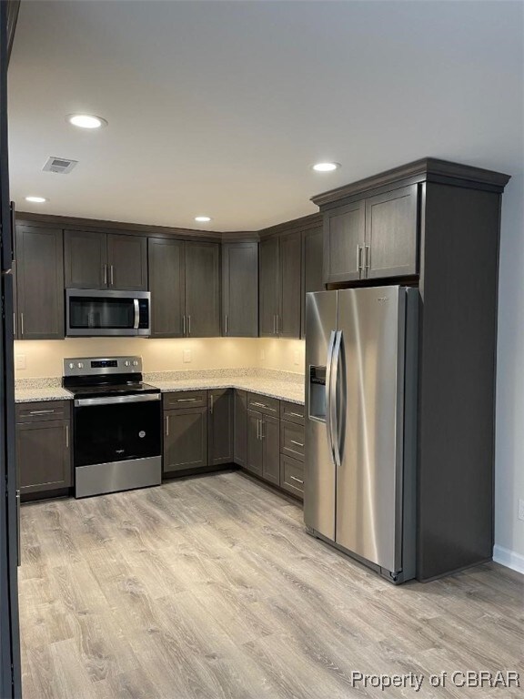 kitchen with appliances with stainless steel finishes, light hardwood / wood-style floors, light stone counters, and dark brown cabinets