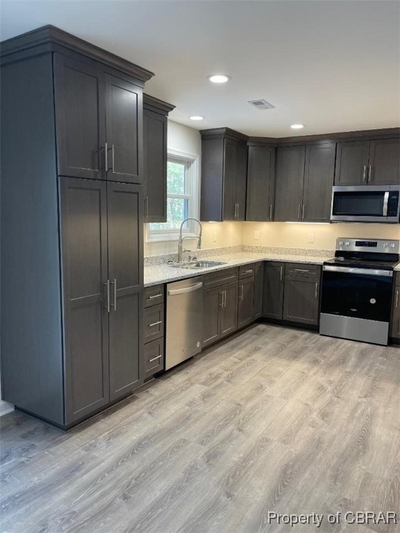 kitchen featuring light stone counters, sink, stainless steel appliances, and light wood-type flooring