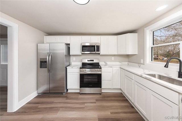 kitchen with light stone countertops, appliances with stainless steel finishes, light wood-type flooring, sink, and white cabinets