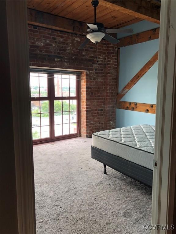 unfurnished bedroom featuring beam ceiling, ceiling fan, carpet, and brick wall