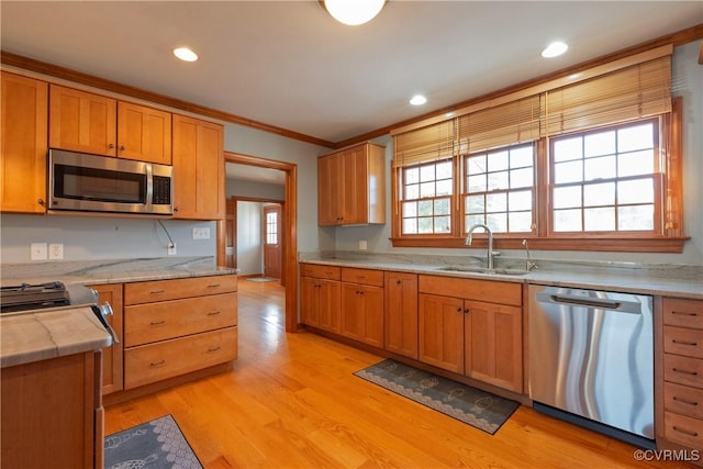 kitchen with light wood-type flooring, stainless steel appliances, ornamental molding, and sink